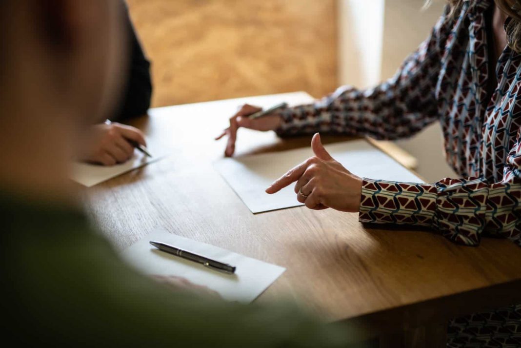 Three people sit around a table with partition action documents on it. One person is a partition lawyer who is explaining the documents to the other two people. 