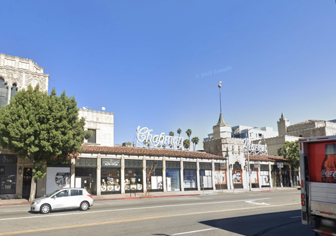 Street view of a historic building with "Chapman Market" signage, large trees, and a clear blue sky.